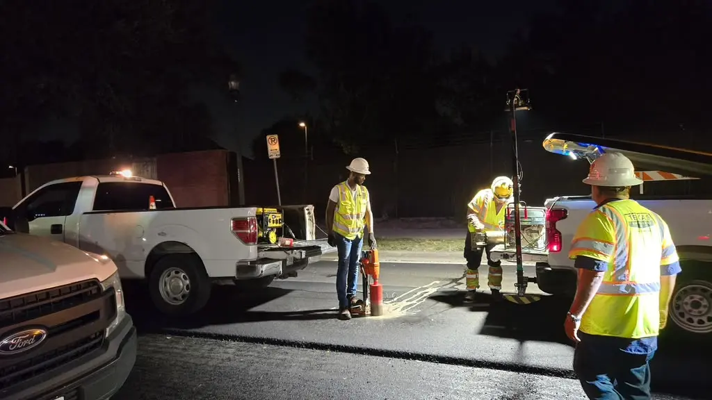 Night coring crew working downtown beside work trucks with light tower